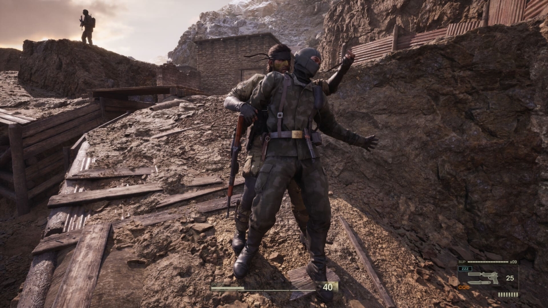 Zwei Soldaten in Militärkleidung auf felsigem Gelände aus Metal Gear Solid Delta: Snake Eater. Ein Soldat hat eine Waffe und ist in einer versteckten Position.