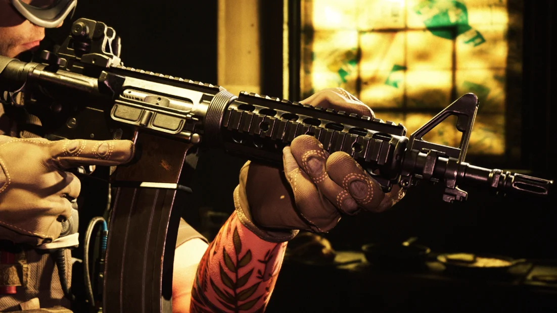 Person wearing tactical gloves holds an Mk18 assault rifle with mounted sight and front grip in firing position.