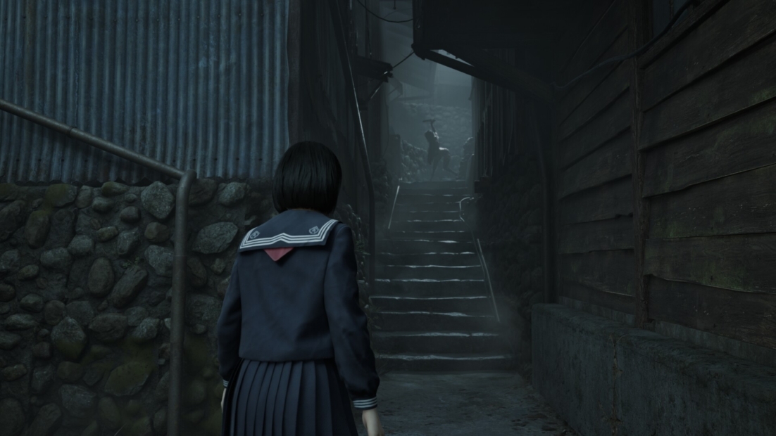 A girl in a dark blue Japanese school uniform stands in a narrow, dark alley looking up at a shadowy figure on a staircase.