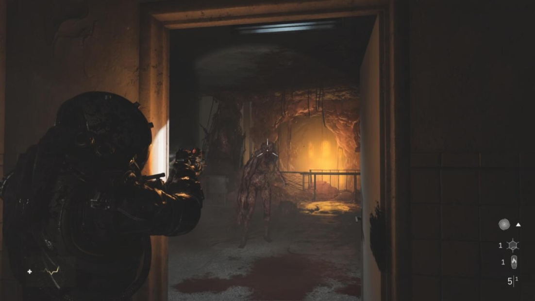 A character in dark armor points a gun towards a monstrous figure in a dimly lit cave-like setting, with orange light illuminating the background.