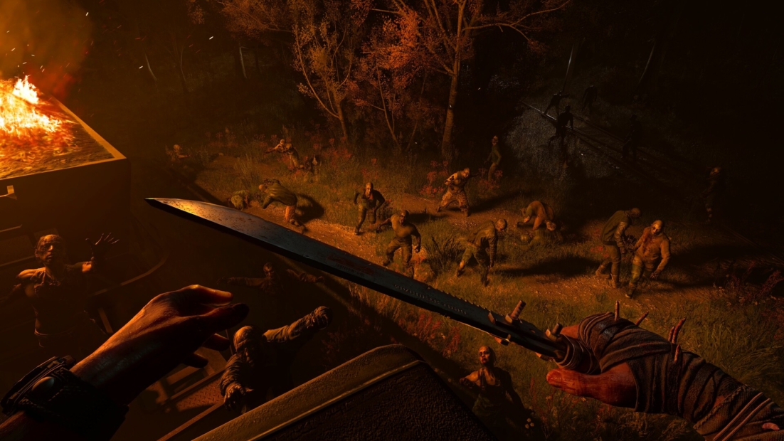 A hand holds a large, serrated sword above a group of zombies standing in the dark. A fire burns in the background, with trees visible.