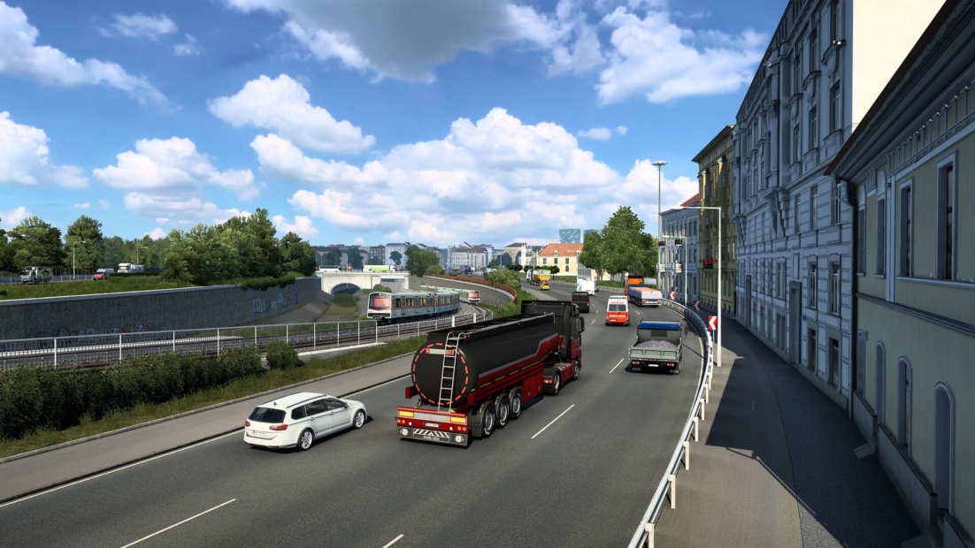 Red and black tanker truck driving on a multi-lane city road in Euro Truck Simulator 2, surrounded by cars and buildings under a partly cloudy sky
