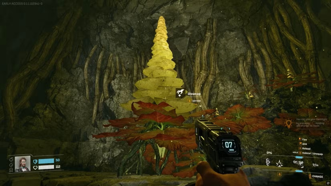 First-person view of a hand holding a pistol aimed at a large yellow conical stalagmite formation in a cave with red plants in the foreground