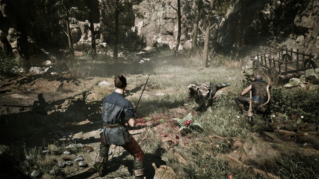 Two men in medieval clothing with weapons stand in a rocky forest clearing with grass and bushes.