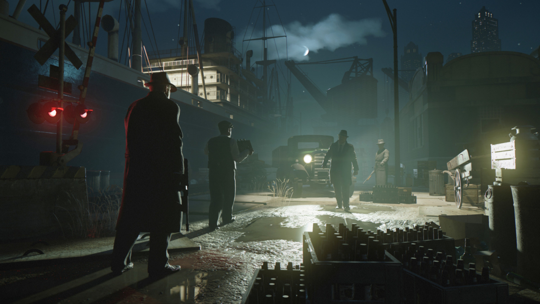 Silhouettes of men in 1930s attire standing on a dock at night with a ship and vintage truck in the background, from Mafia: Definitive Edition