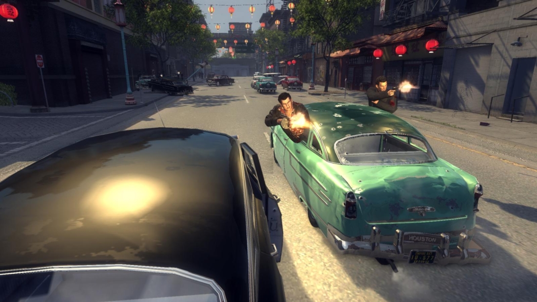 Two men firing pistols from a green vintage car driving through a city street decorated with red lanterns, from the game Mafia II (2011)