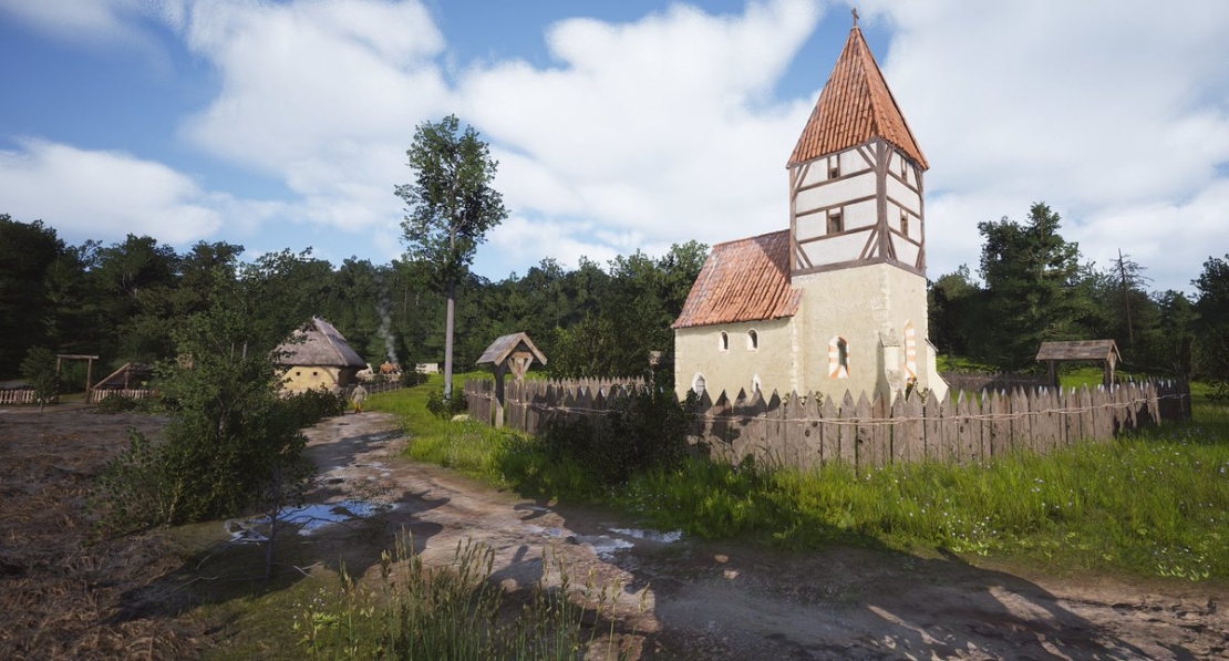 White half-timbered building with pointed red roof, surrounded by wooden fence, on grassy area with trees and a path in front.