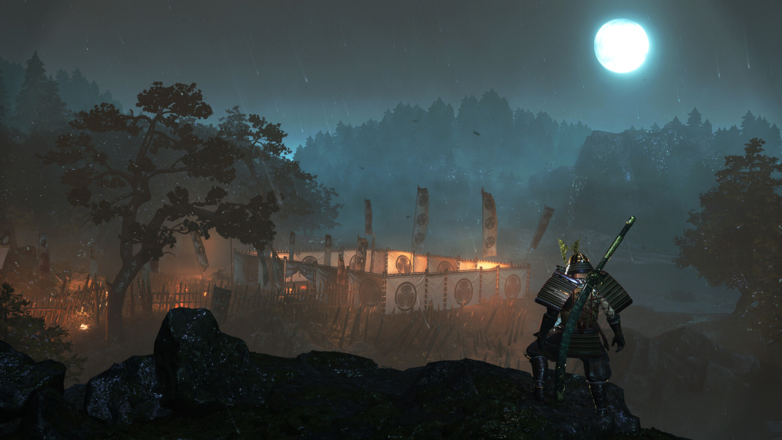Warrior in traditional armor stands on rocks looking at a lit camp with flags surrounded by trees under a full moon
