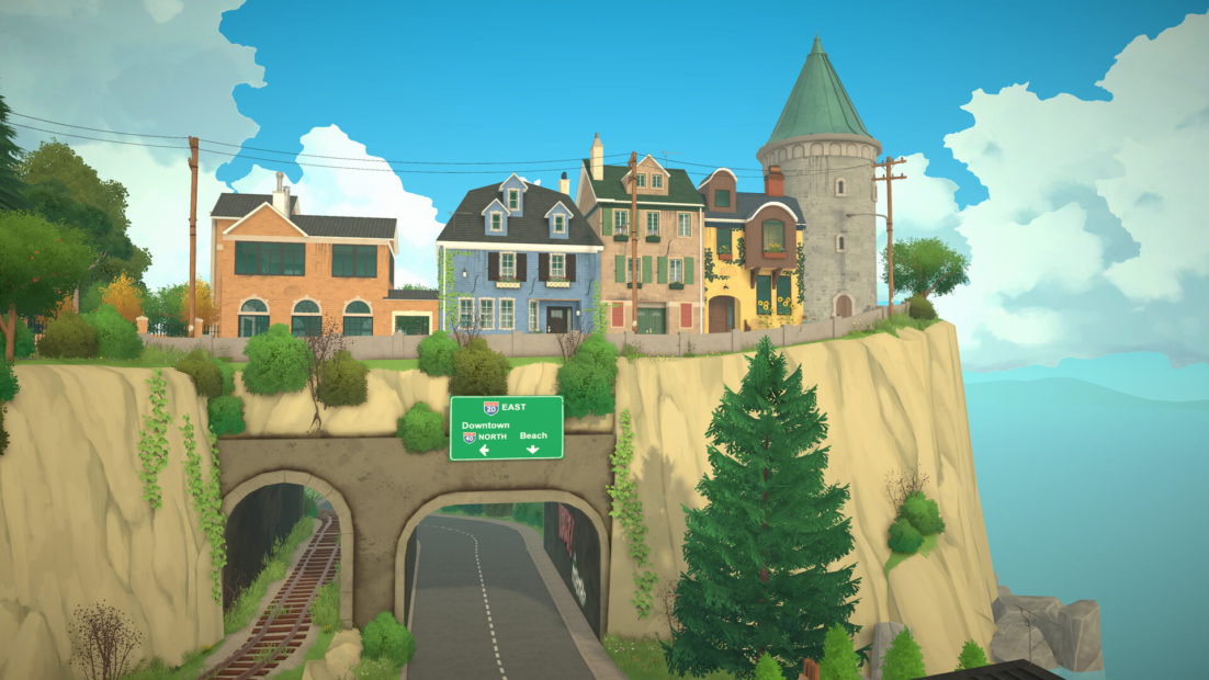 Small town with colorful houses and a round tower on a cliff above a road with a tunnel and railway track