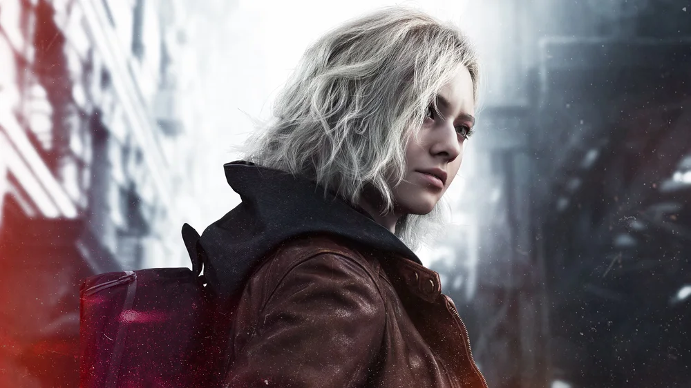 Person mit schulterlangem, gewelltem Haar trägt eine braune Jacke und einen schwarzen Rucksack in einer urbanen Umgebung.