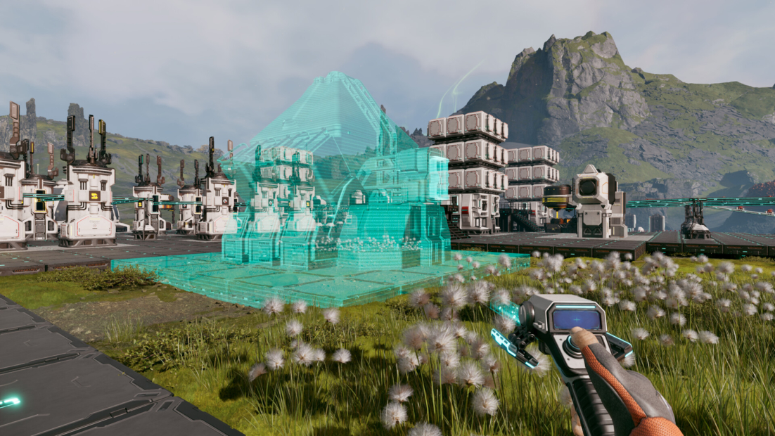 Video game scene showing a hand holding a futuristic weapon in the foreground, with a green transparent 3D hologram structure on grass, and futuristic machines and mountains in the background.
