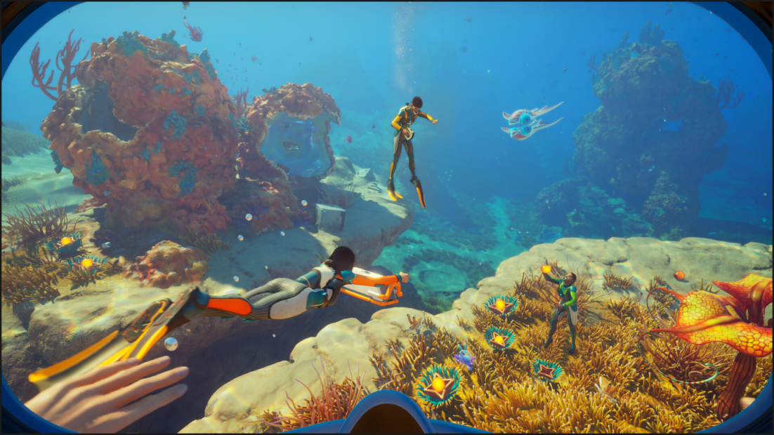 Underwater view through diving goggles showing three divers in wetsuits swimming among coral and marine life