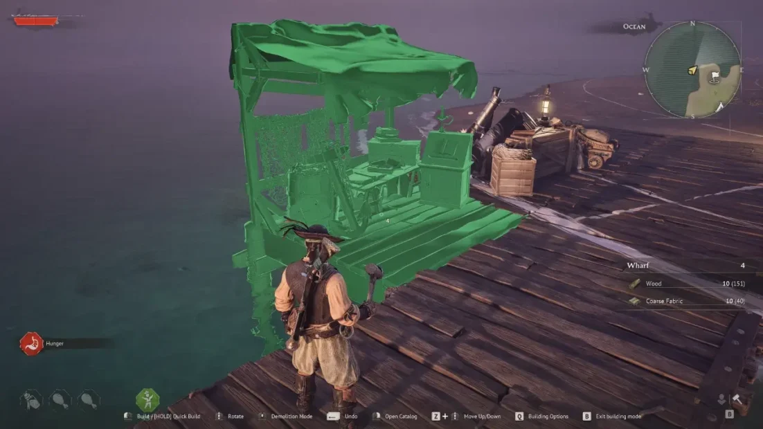 Game character in pirate clothing stands on a wooden pier next to a small green covered stall with crates and barrels